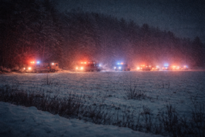 a grainy image of a line of emergency vehicles off in the distance parked along a snowy field